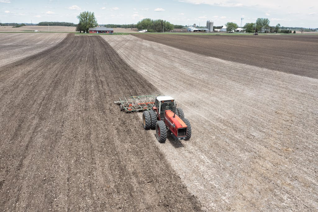 A drone captures a tractor plowing fields on a spring day, showcasing agriculture in Minnesota.