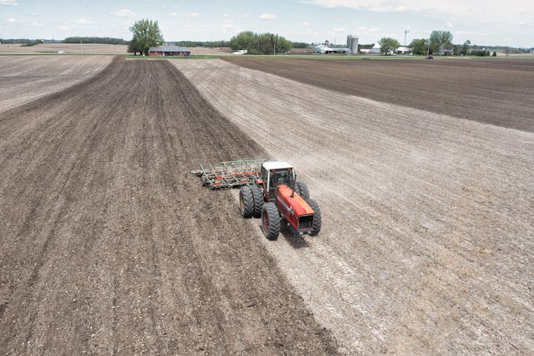 A drone captures a tractor plowing fields on a spring day, showcasing agriculture in Minnesota.