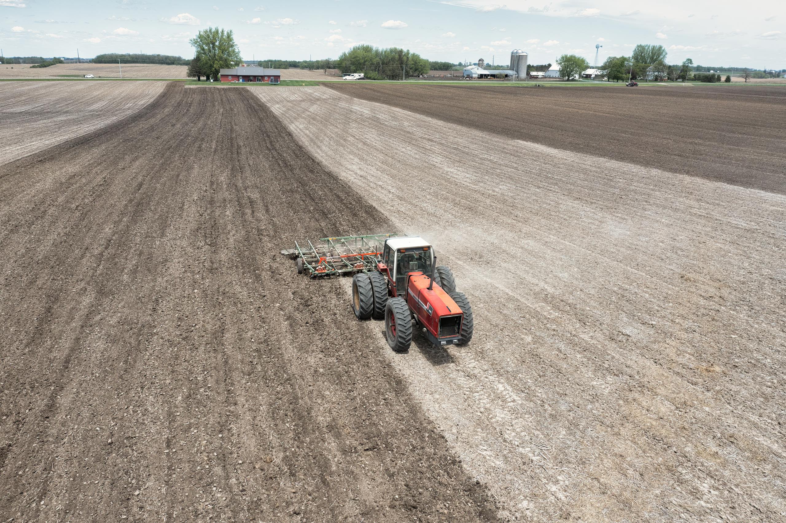 A drone captures a tractor plowing fields on a spring day, showcasing agriculture in Minnesota.