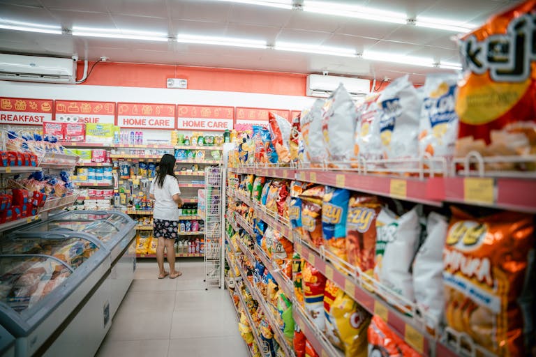 A woman browsing snack shelves at a supermarket, surrounded by various chips packages.
