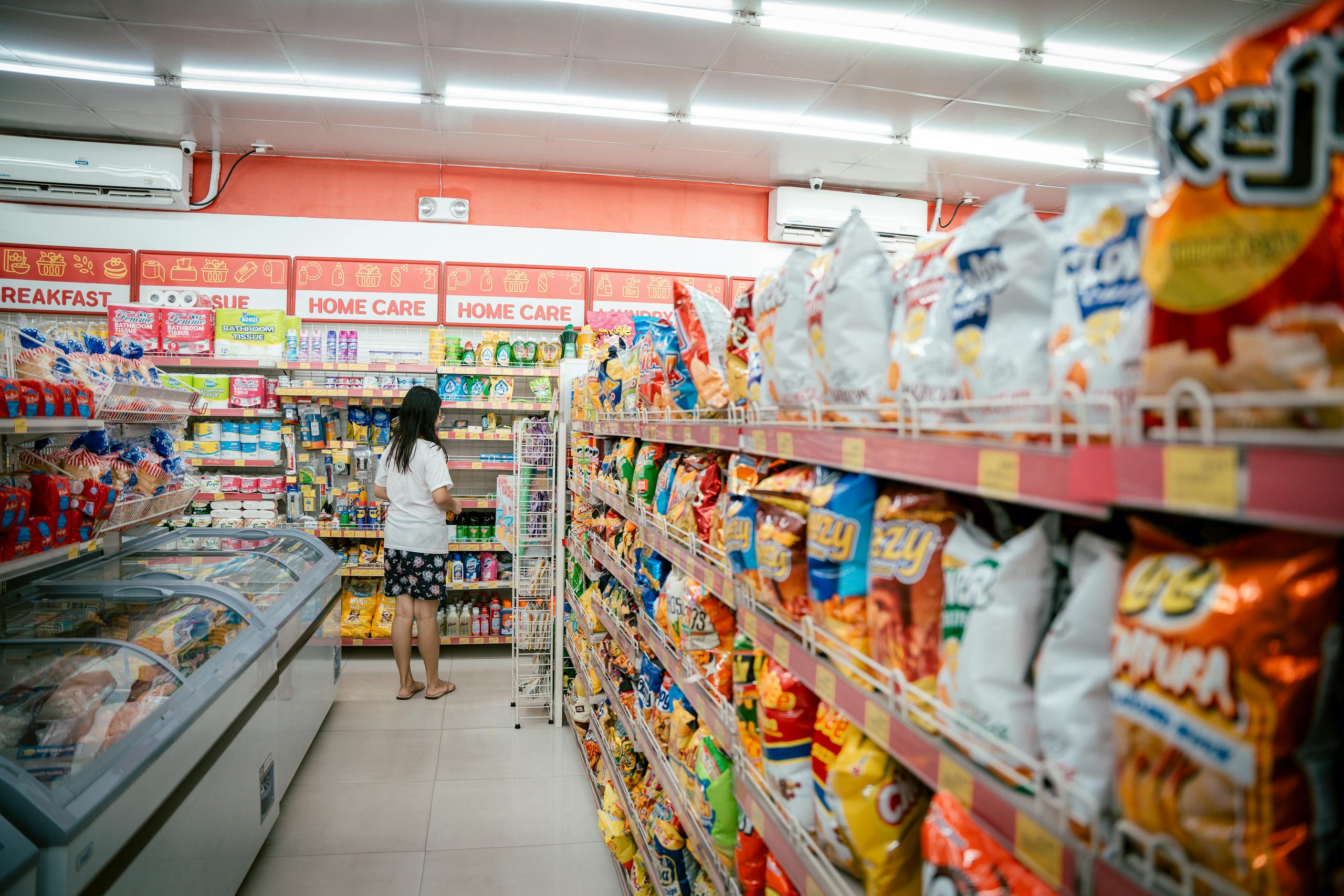 A woman browsing snack shelves at a supermarket, surrounded by various chips packages.