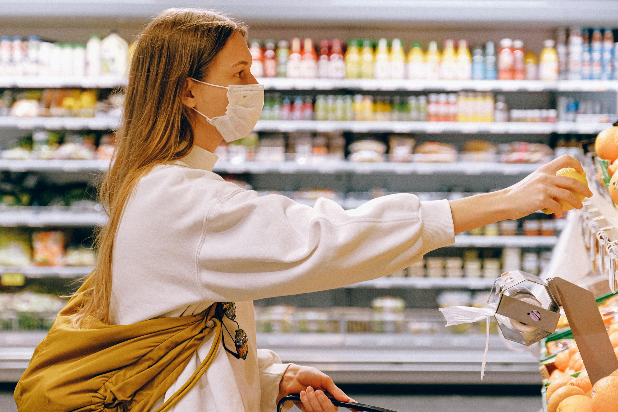 Woman wearing a face mask while selecting fruit in a supermarket.