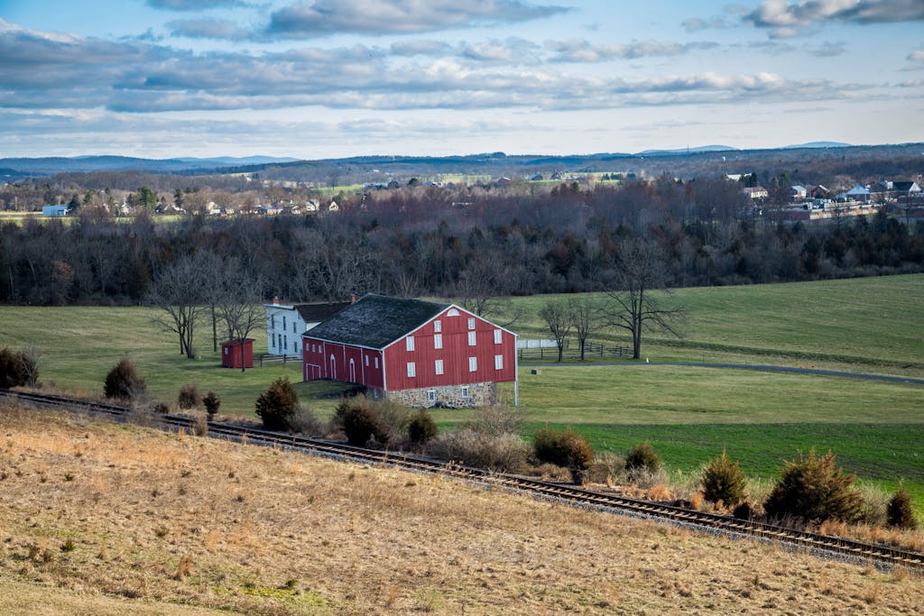Picturesque red barn on farmland amidst rolling hills and clear skies.