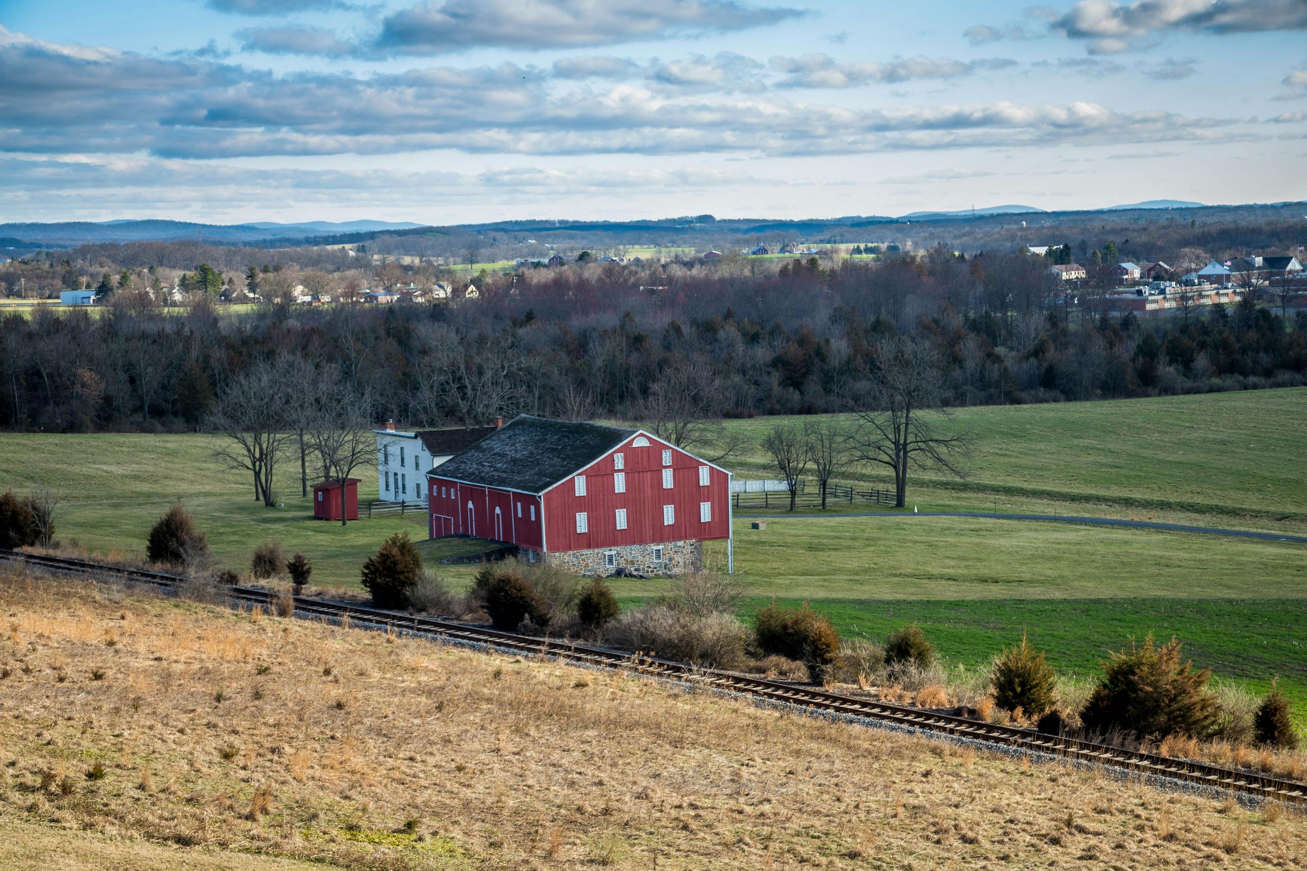 Picturesque red barn on farmland amidst rolling hills and clear skies.