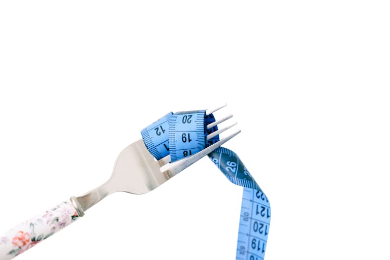 A fork entwined with a blue measuring tape, symbolizing dieting and weight management.
