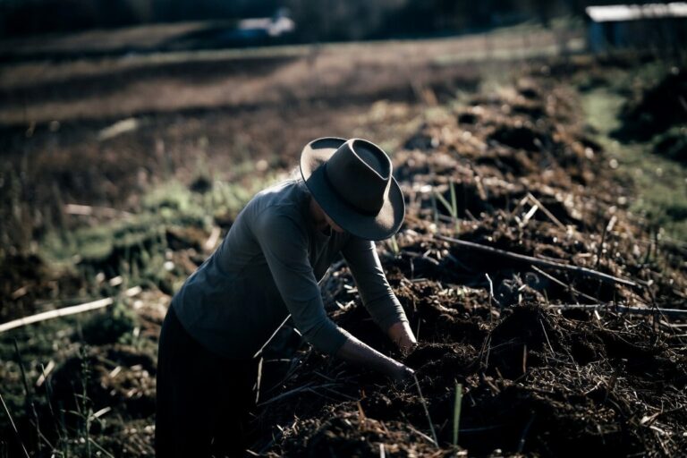 An AI-generated image of a woman in a wide-brimmed hat, head bowed and face unseen, intently working with both hands in a no-dig garden bed.