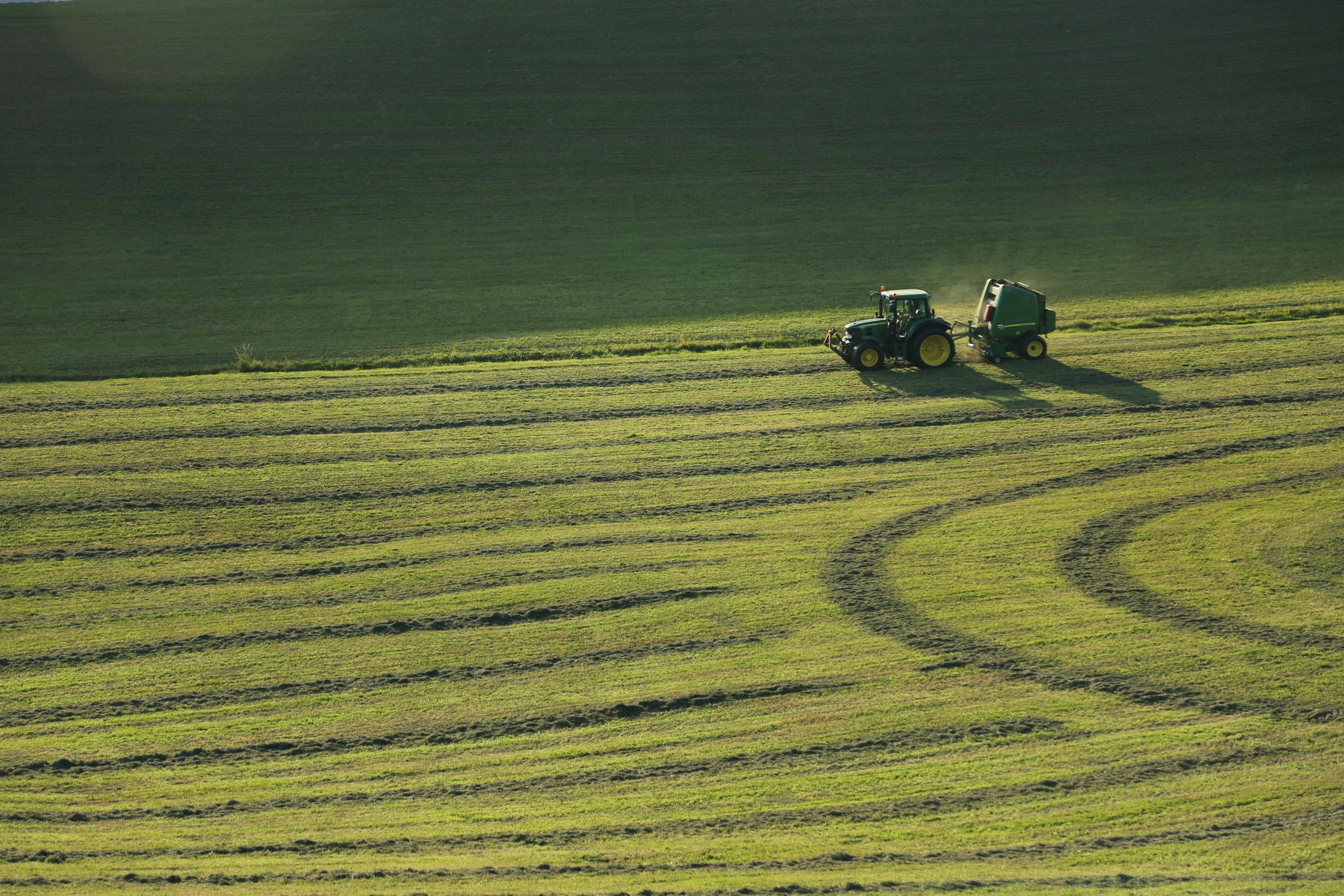A tractor plows a lush green field, creating geometric patterns in spring.