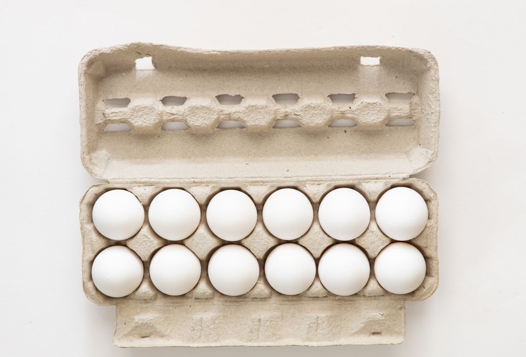 Minimalist flat lay of white eggs in a carton tray, perfect for culinary or health concepts.