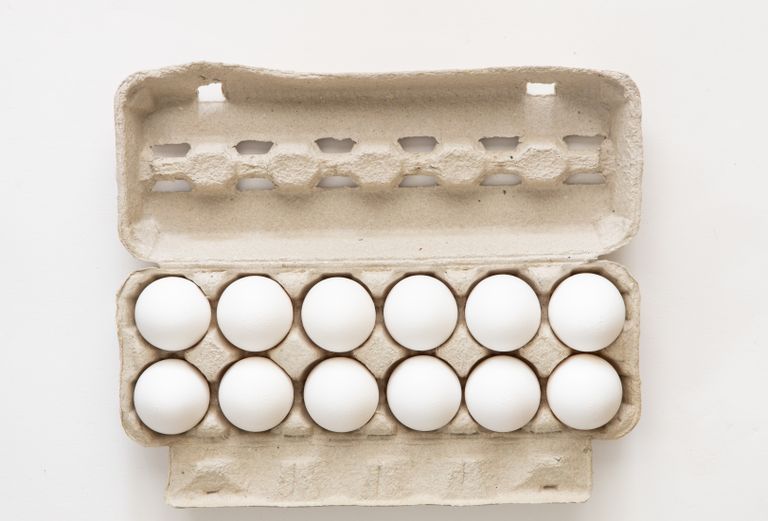 Minimalist flat lay of white eggs in a carton tray, perfect for culinary or health concepts.