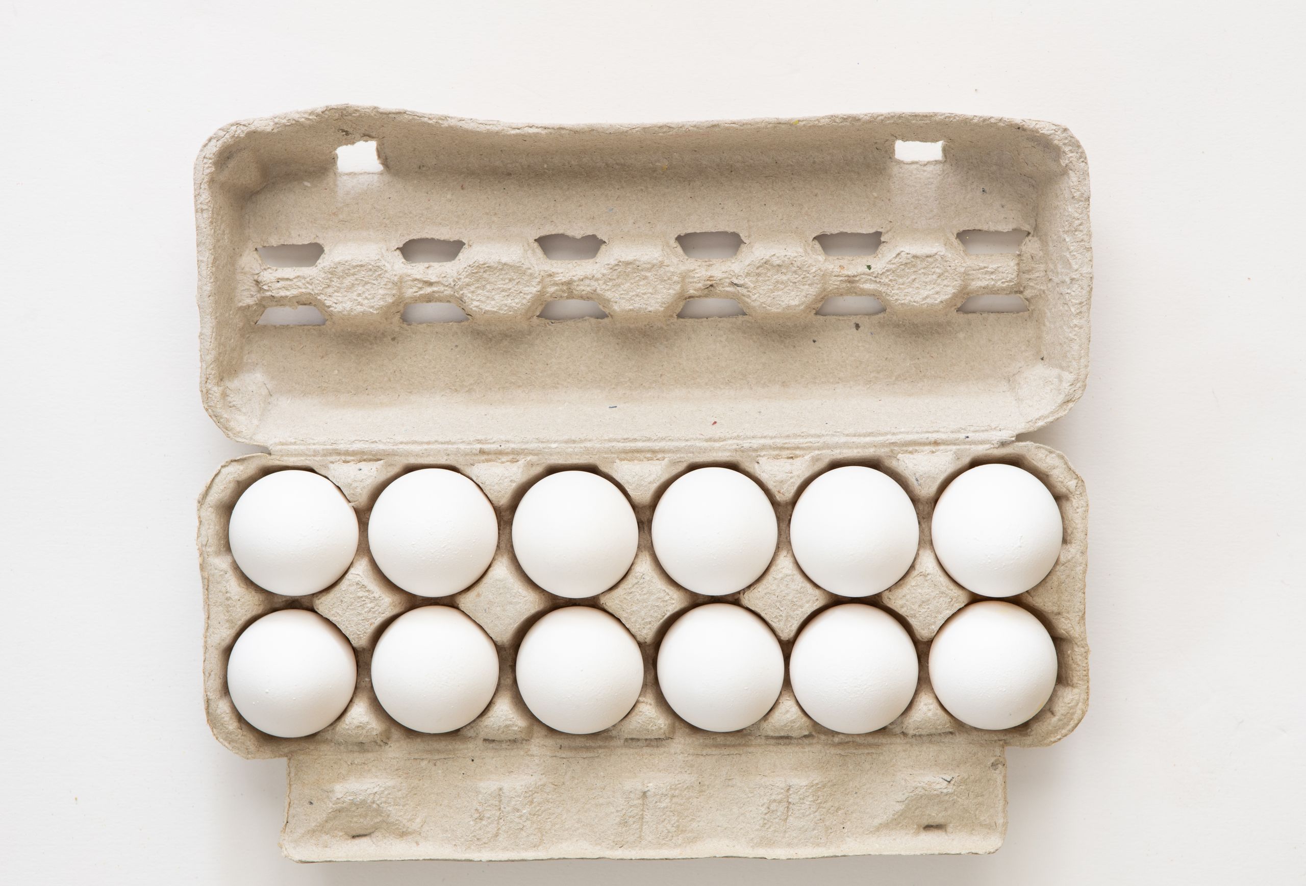 Minimalist flat lay of white eggs in a carton tray, perfect for culinary or health concepts.