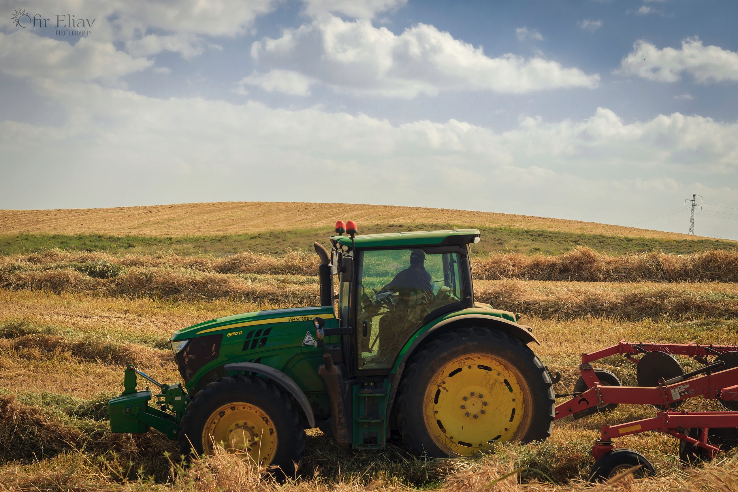 A green tractor working in a hay field with blue skies during harvest season.