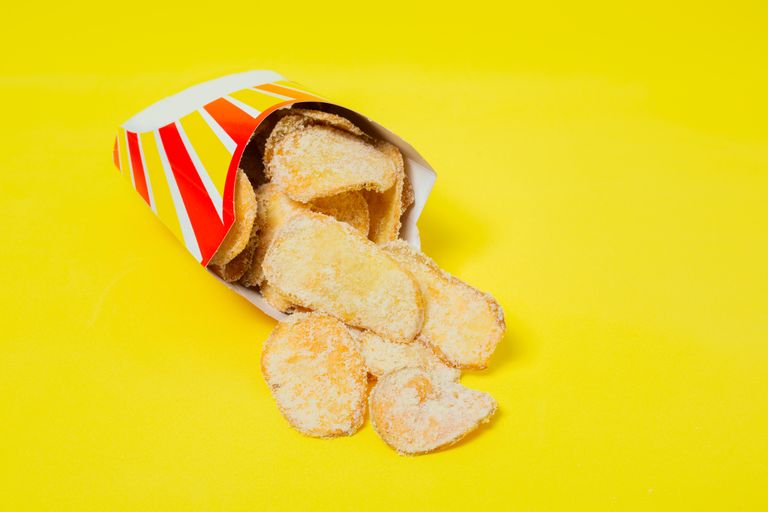 From above of tasty crispy potato chips served in colorful cardboard box placed on bright yellow surface