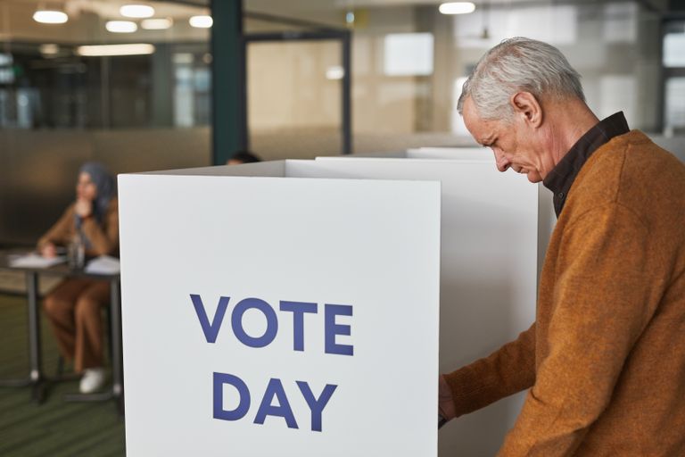 Senior man in brown sweater voting at an indoor polling station on election day.