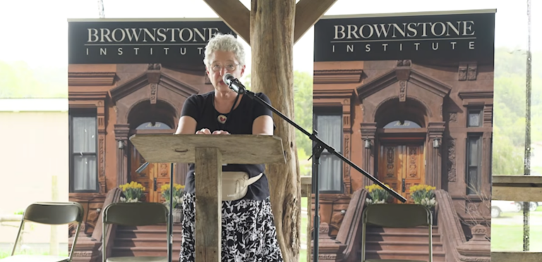 Meryl Nass stands at a podium with Brownstone Institute banners behind her