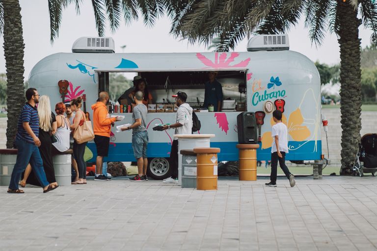 People gather at a colorful food truck, enjoying a lively outdoor setting.