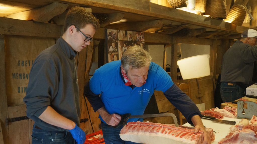 Two butchers meticulously preparing cuts of meat in a rustic indoor setting, showcasing skill and detail.