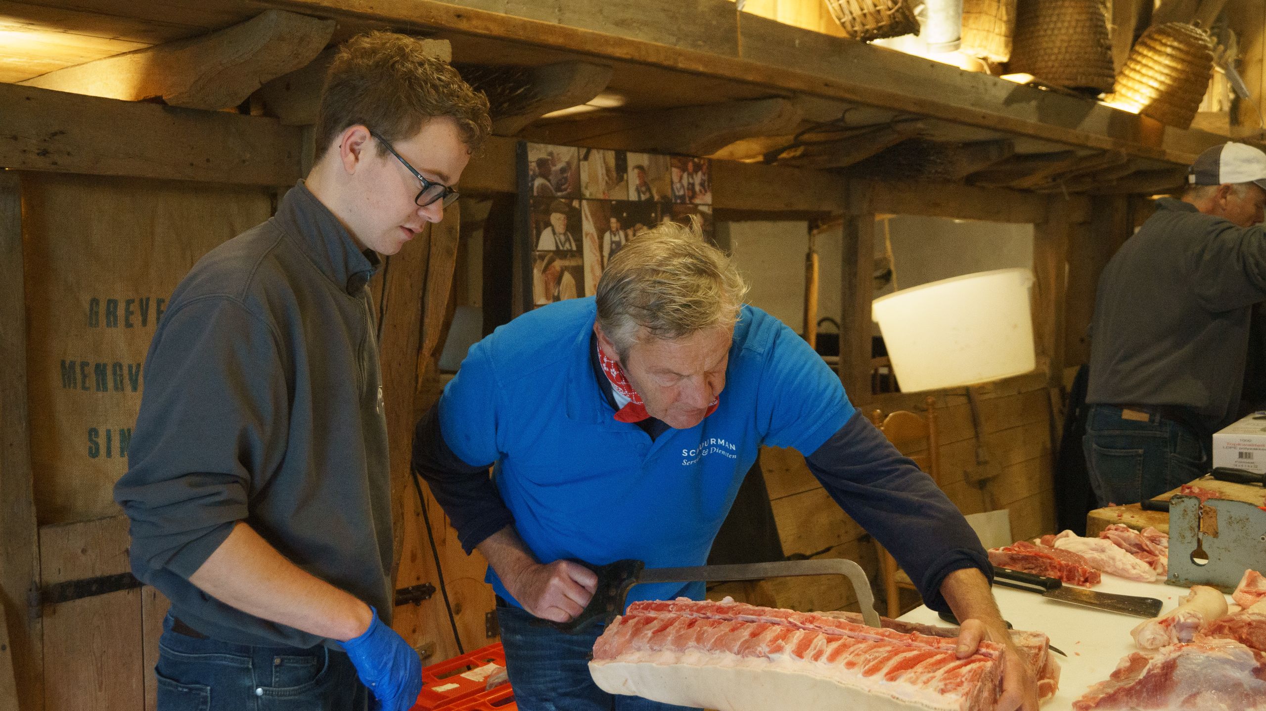 Two butchers meticulously preparing cuts of meat in a rustic indoor setting, showcasing skill and detail.